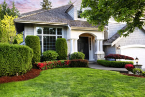 Beautiful home with manicured green lawn and blooming red flowers in bushes serviced by landscaping company